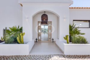 Entrada elegante ao estilo do Algarve, com porta em arco, texturas naturais, iluminação marcante e paisagismo escultural inspirado no deserto