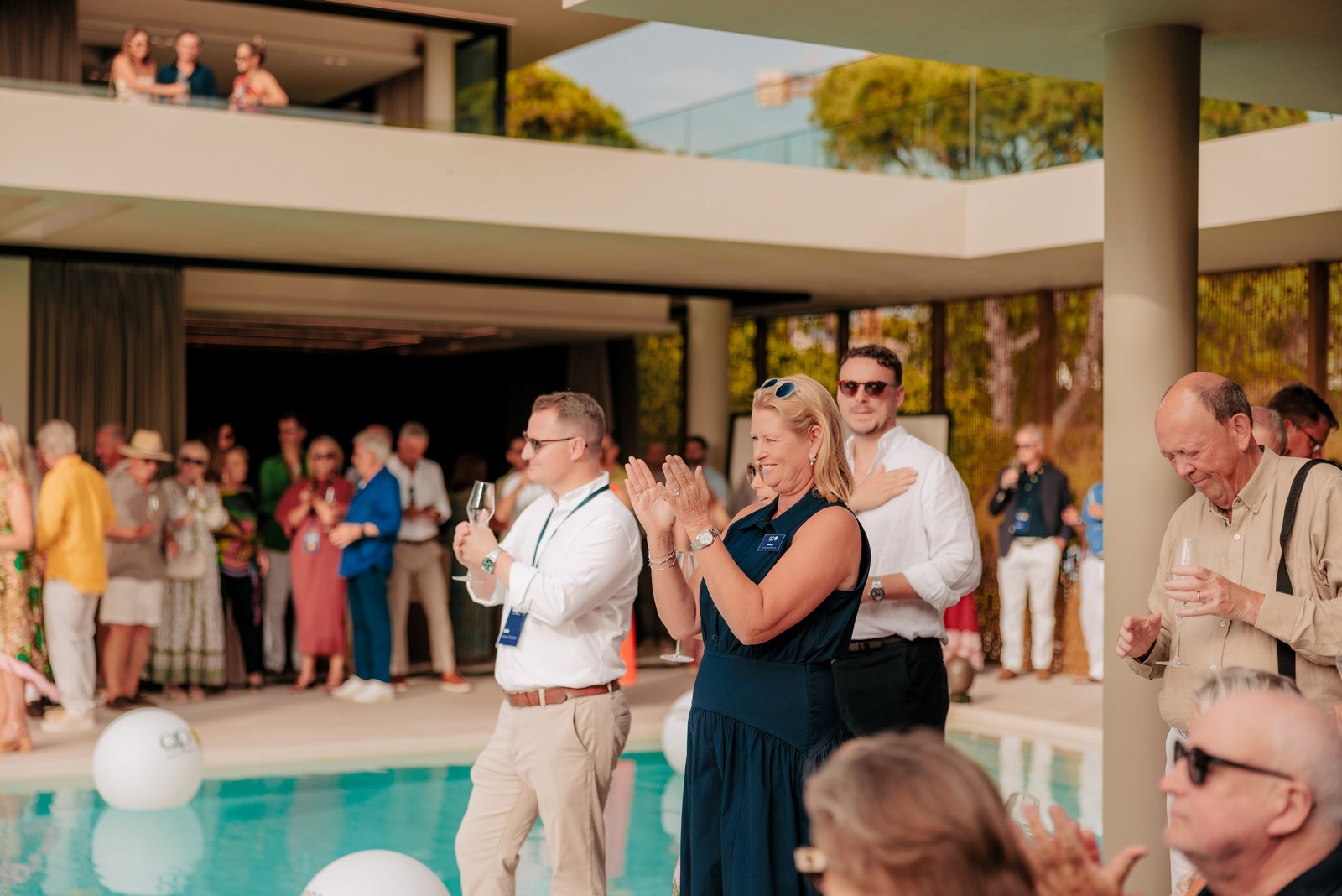 Gäste applaudieren auf der Terrasse am Pool während der Reden auf der QP Savills-Sommerparty