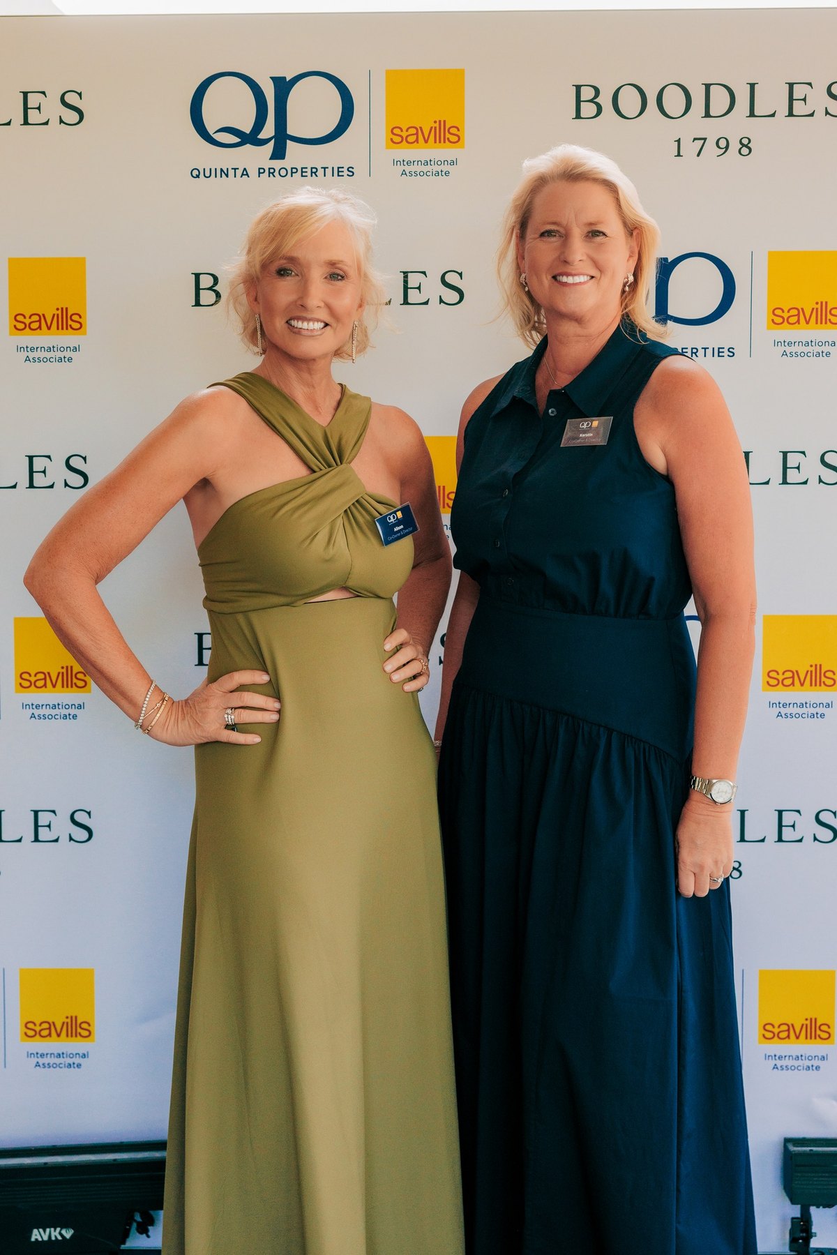 Zwei Gäste vor der Kulisse von QP Savills und Boodles am Eingang zur Party
