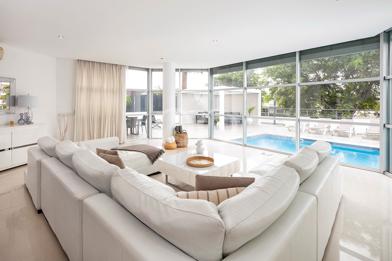 Helles Wohnzimmer mit großen Fenstern und Blick auf den Swimmingpool
