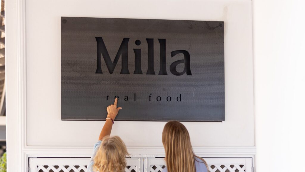 Alison et Milla sous l'enseigne « Milla Real Food » à l'entrée du café à Almancil