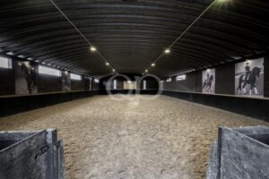 Spacious indoor equestrian riding arena with sand surface and overhead lighting